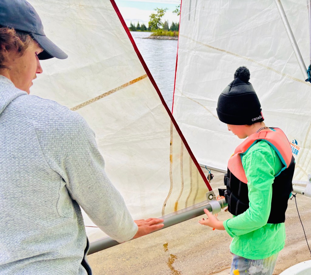 A sailing coach teaching a boy how to attach a sail