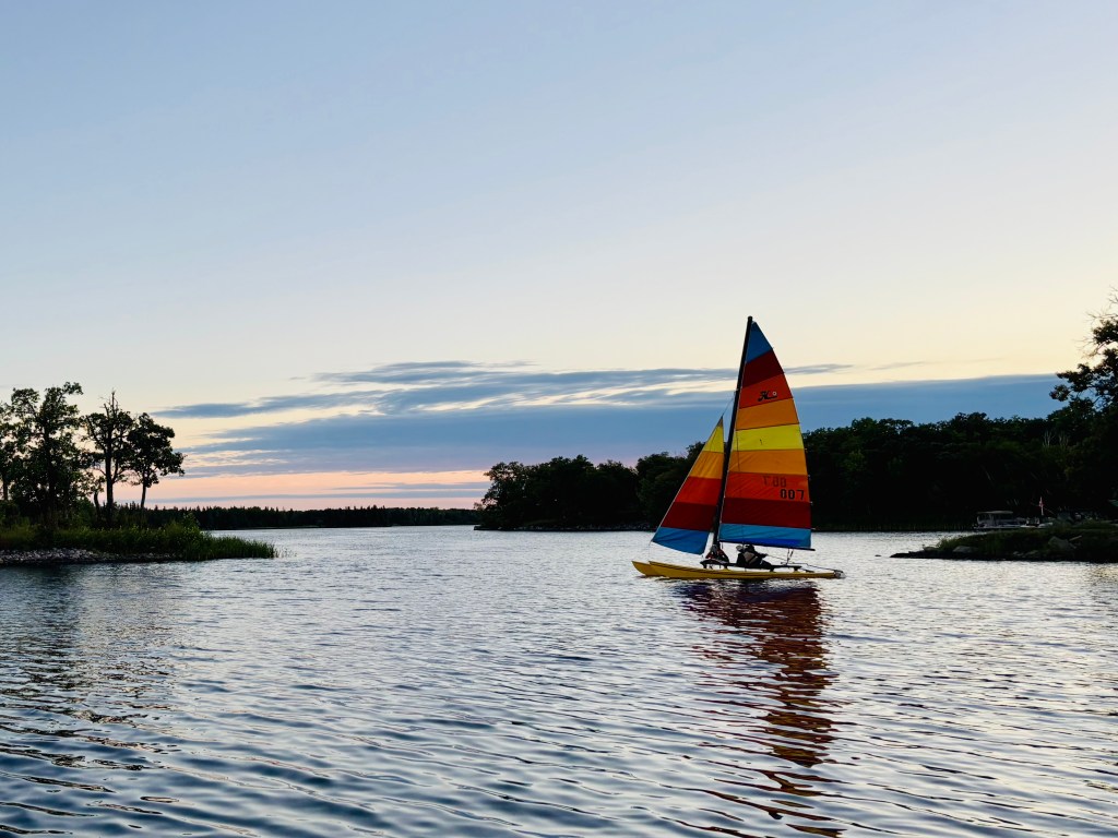 A catamaran sailing on a river at sunset