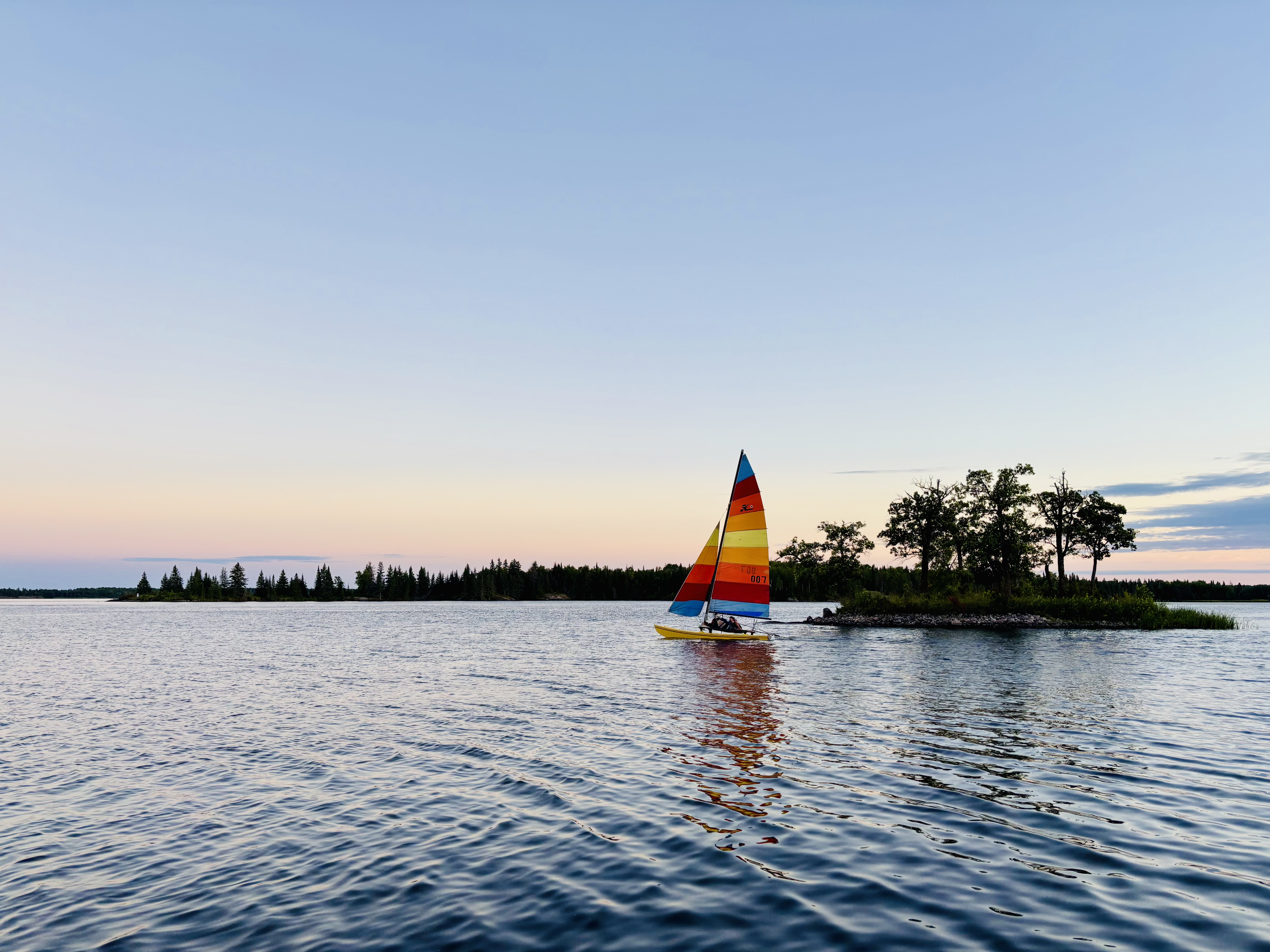 A Hobie 16 Catamaran Sailing past an island at sunset in Manitoba