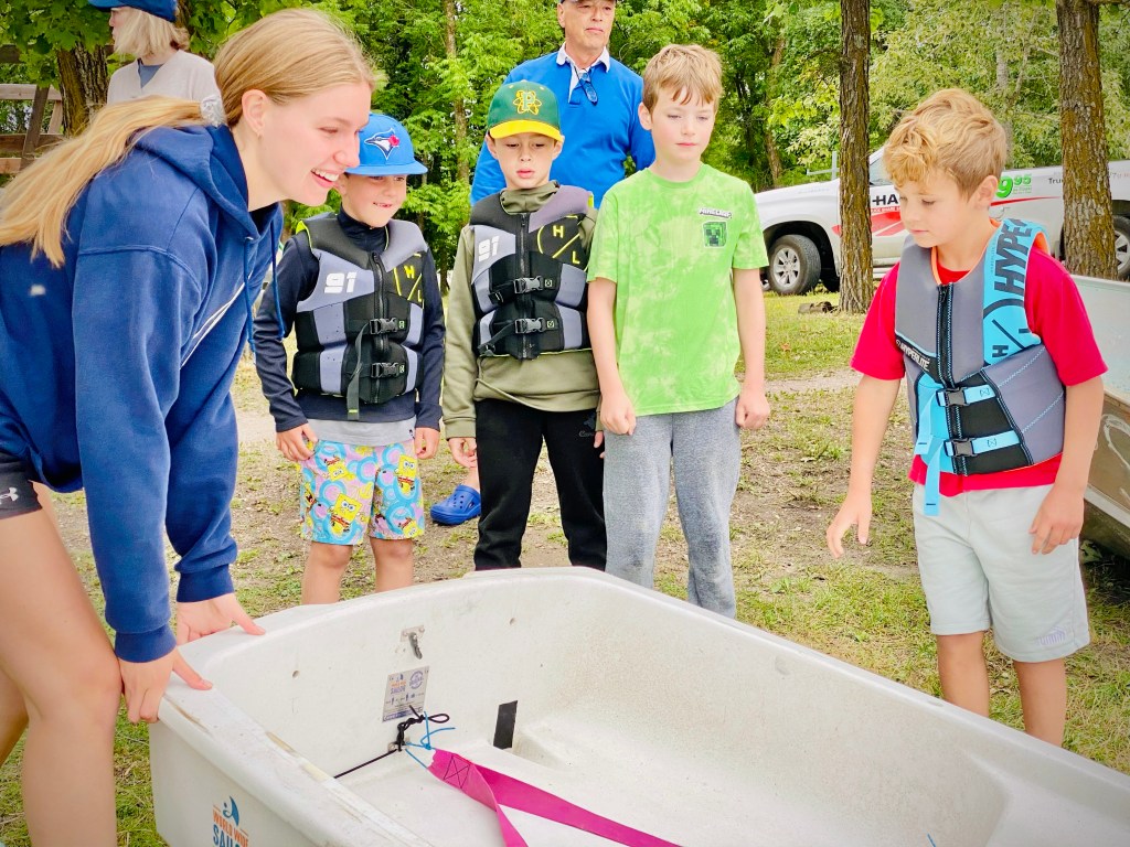 Female sailing coach demonstrating a boat to a group of boys