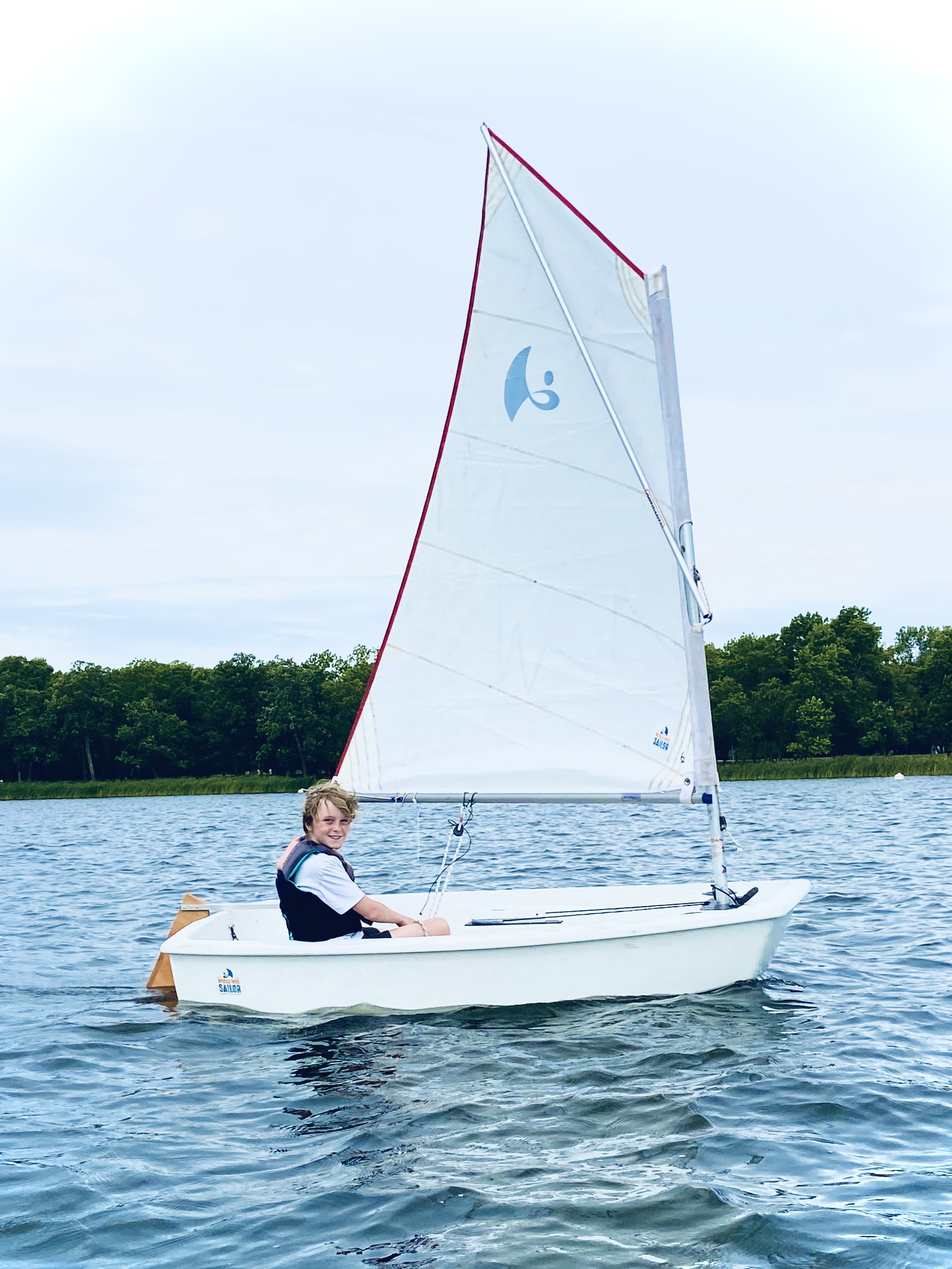 A smiling boy sailing an Opti